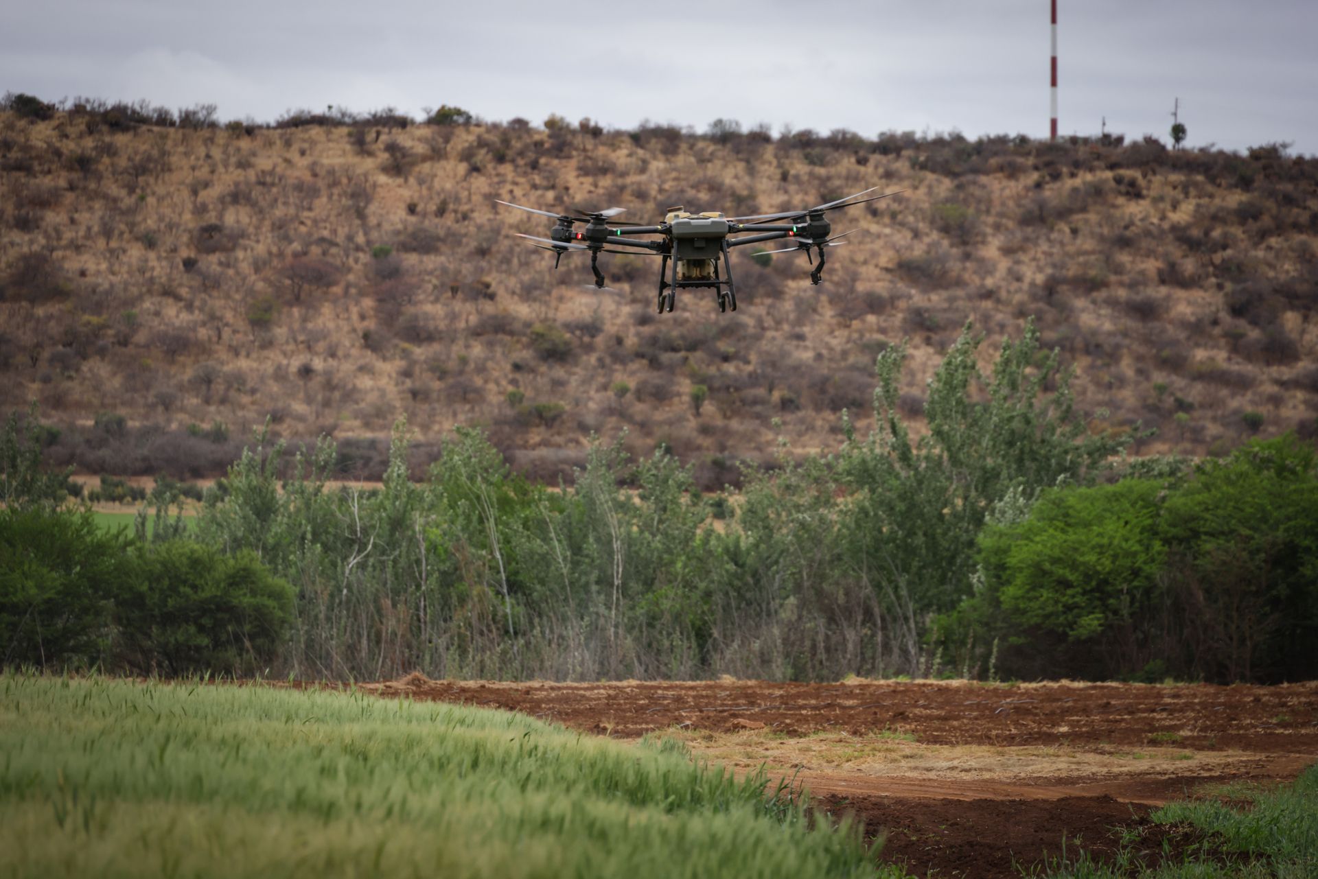 Multirotor drone flying over fields and hillside vegetation